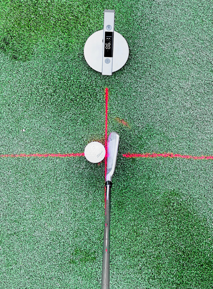 Golf club, golf ball, and digital device on a green surface with red lines.