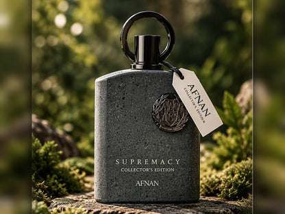 A dark gray stone-textured bottle with a black loop cap and a cream hangtag reading AFNAN Collector's Edition, set outdoors on a mossy log with a blurred green forest background.